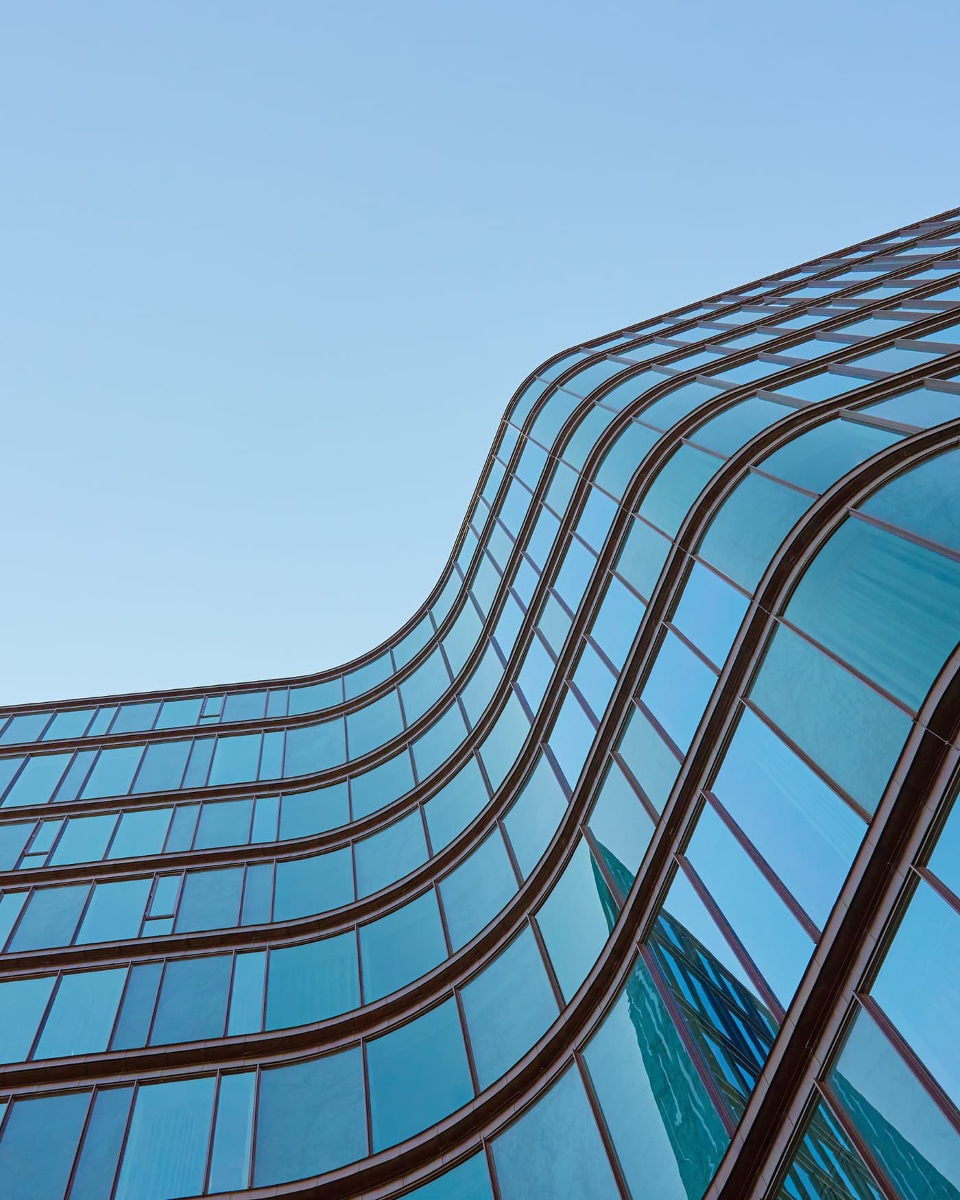 Contre-plongée sur la façade de verre incurvée d'un immeuble contemporain, détachée sur un ciel dégagé