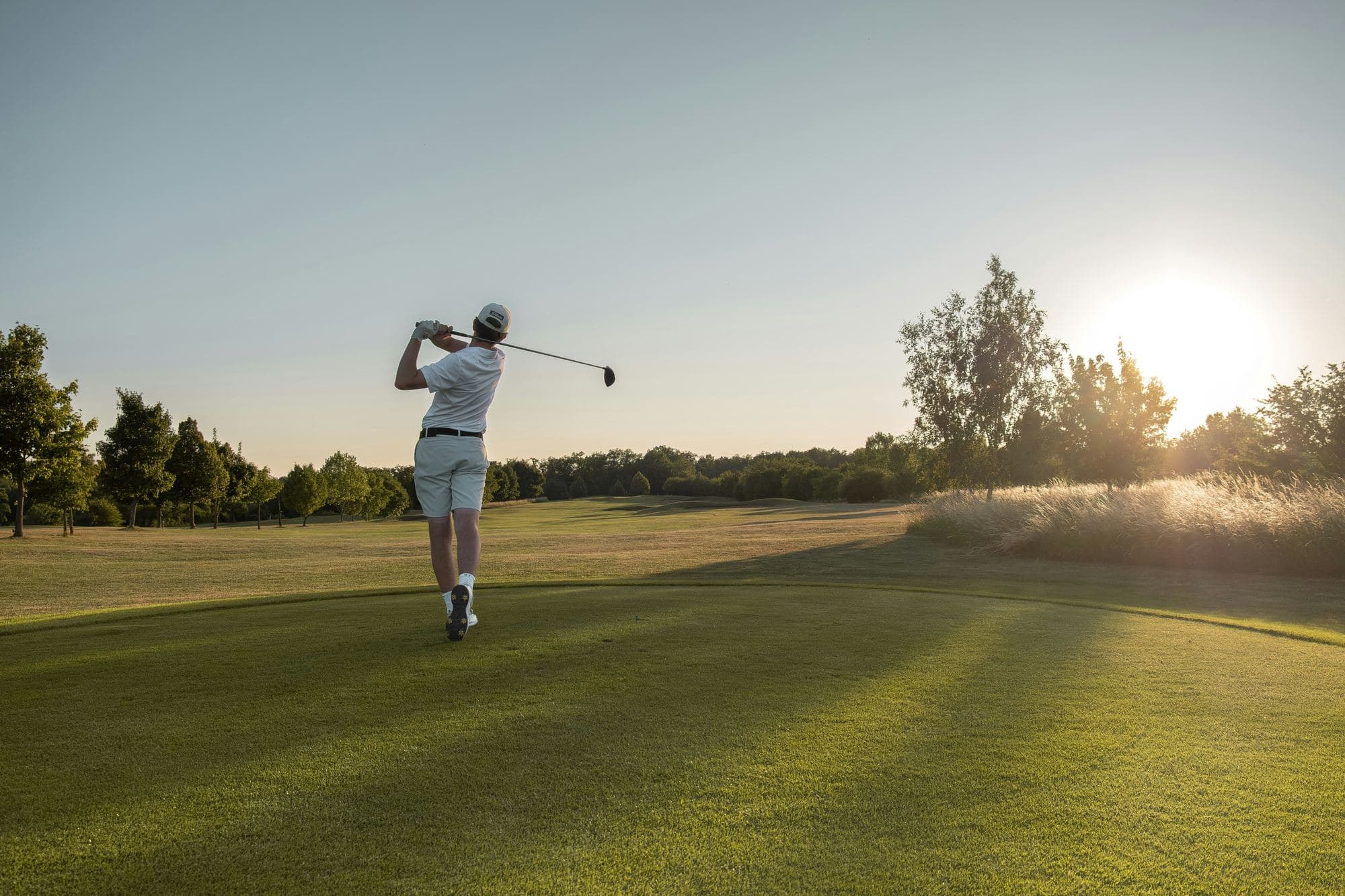 Le parcours de golf 18 trous au lever du jour, un joueur en plein swing